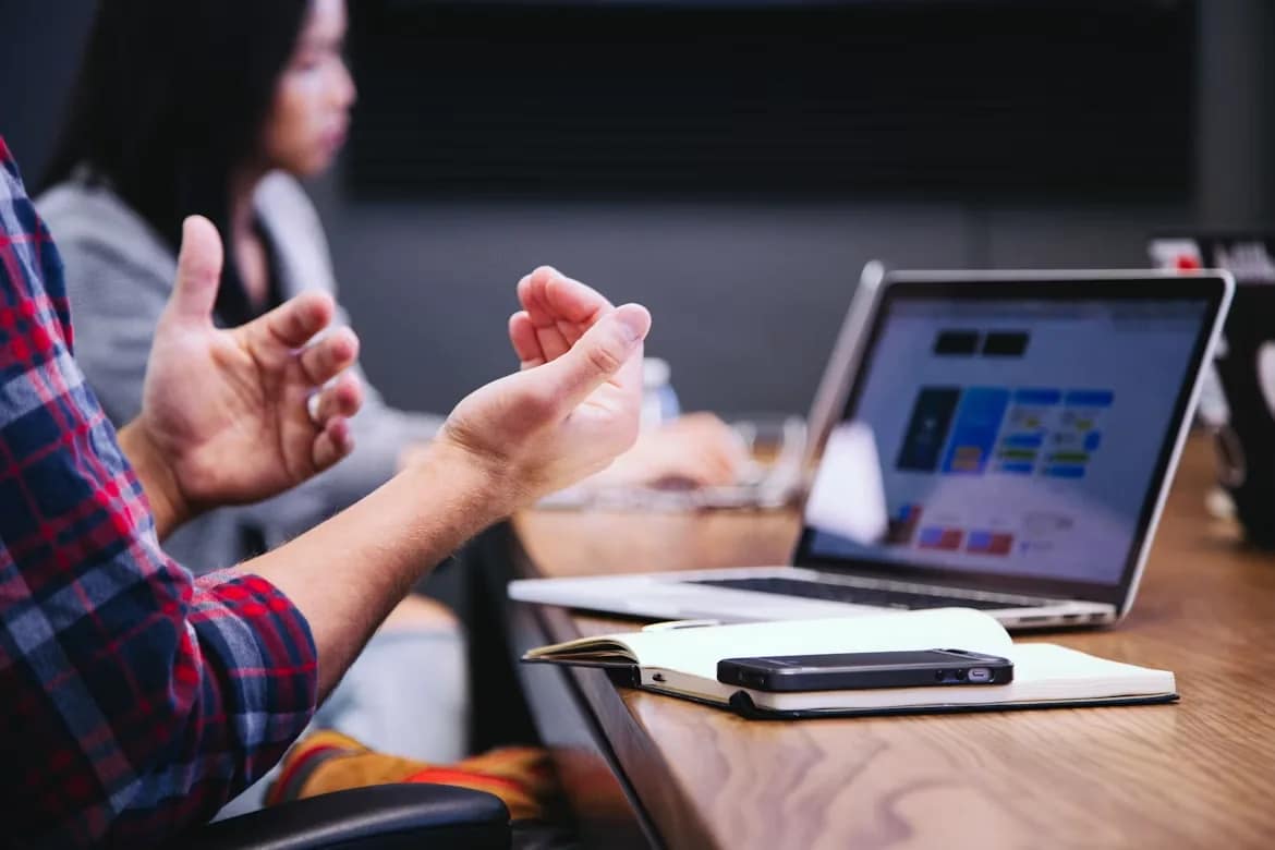 Deelnemers in gesprek tijdens een sessie, met laptop en notitieblok op tafel