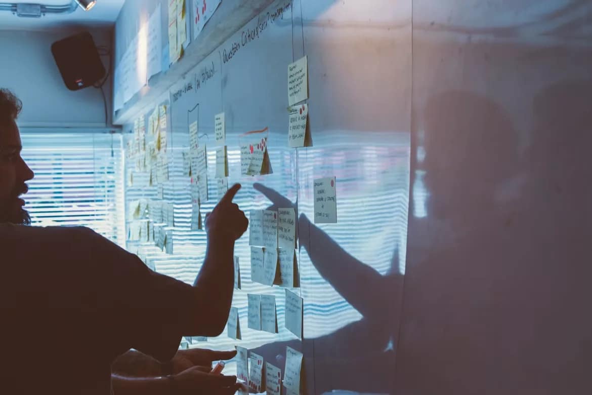 Twee mensen wijzen naar een wand met post-its tijdens een strategiesessie